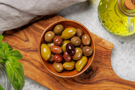 An assortment of various olives presented in a bowl and olive oil bottle, showing different colors, textures, and flavorsの写真素材