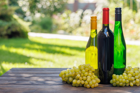 Wine bottles with grapes on a wooden table, glowing with sunny bokeh in the background and copy spaceの写真素材