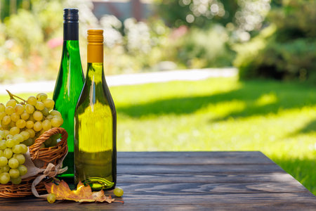Wine bottles with grapes on a wooden table, glowing with sunny bokeh in the background and copy spaceの写真素材
