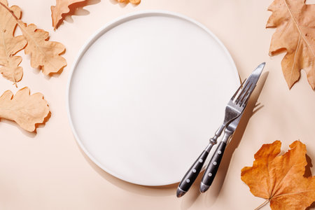 Empty plate on beige background surrounded by autumn yellow leaves, seasonal food mockup. Flat layの写真素材