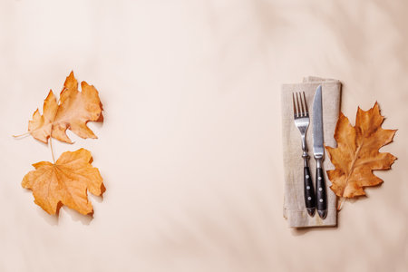 Empty space on beige background with silverware surrounded by autumn yellow leaves, seasonal food mockup. Flat layの写真素材