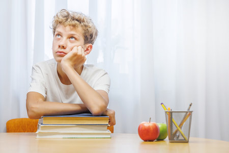 Schoolboy studying at home with notebook, and learning materials, looking thoughtful and confusedの写真素材