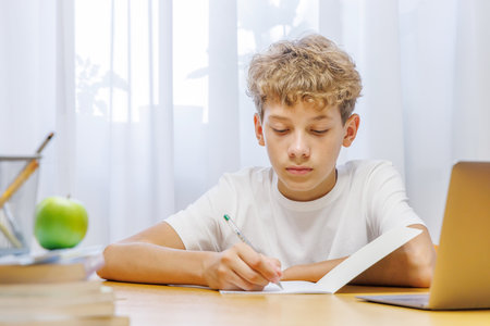 Schoolboy sitting at home, studying with focus and concentration while doing homeworkの写真素材