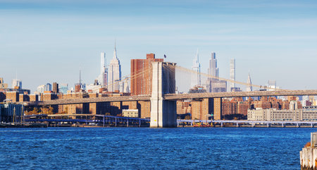 The New York Manhattan bridge skyline during autumn, with iconic skyscrapers framed by golden and...