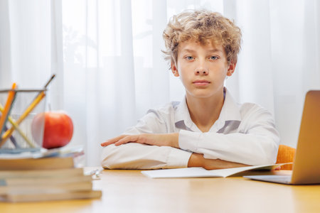 Schoolboy studying at home with laptop, notebook, and learning materials