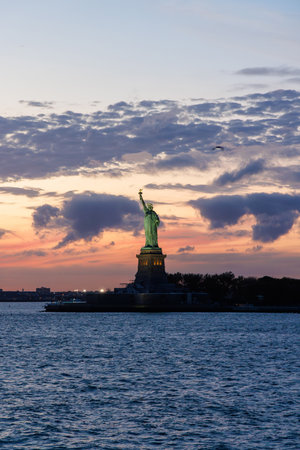 Statue of Liberty at sunset with dramatic sky and warm golden light reflecting on the monument