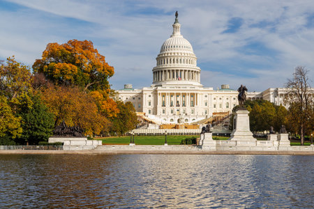 The US Capitol in Washington, DC, surrounded by vibrant autumn foliage. Golden and crimson leaves...