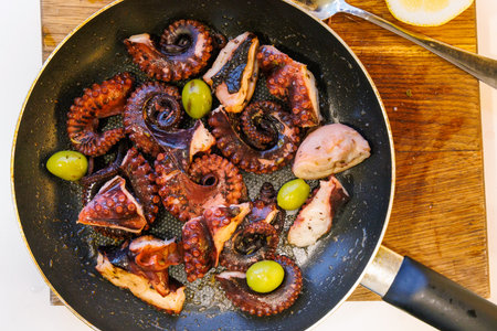 Fried octopus in olive oil with olives and wine served in a pan. Flat layの写真素材