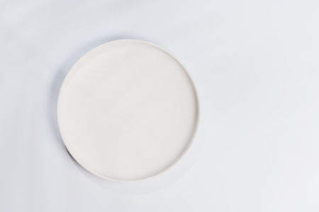 Empty plate on a white background with leaf shadows, perfect food mockup. Flat lay with copy spaceの写真素材