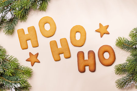 Ginger cookies shaped as Ho Ho Ho with fir branches on beige background, Christmas card styleの写真素材
