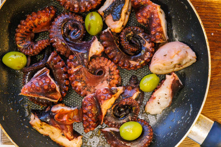 Fried octopus in olive oil with olives and wine served in a pan. Flat layの写真素材