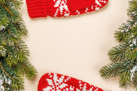 Christmas card with fir branches and mittens on beige surface, festive holiday with copy spaceの写真素材