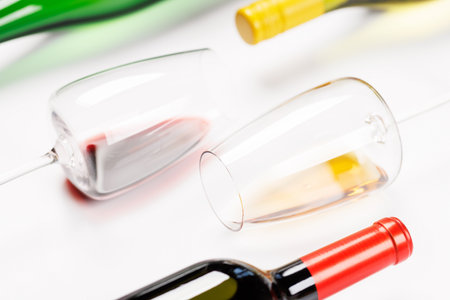 Wine glasses with red and white wine and bottles lying on white background, minimal elegant style with copy spaceの写真素材