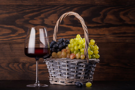 Red wine glass and basket of fresh grapes on a table against a stone wallの写真素材