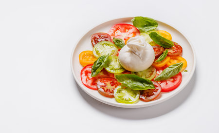 Fresh burrata served on slices of colorful tomatoes, drizzled with olive oil and herbsの写真素材