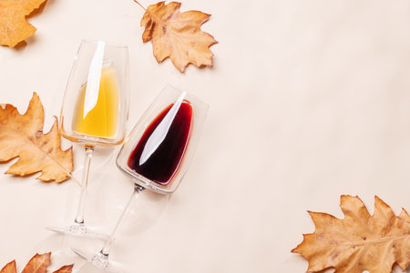 Wine glasses with autumn leaves on beige background, fall composition with copy spaceの写真素材