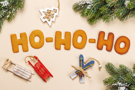 Ginger cookies shaped as Ho Ho Ho with fir branches on beige background, Christmas card style