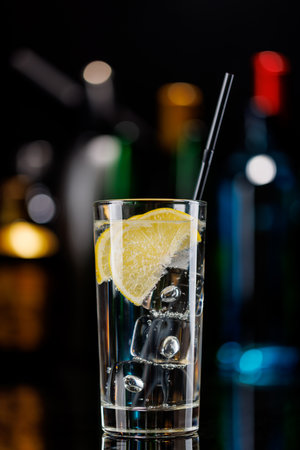 Gin tonic cocktail on a bar table. The colorful bokeh of illuminated bottles in the background enhances the mood, creating a dynamic and lively ambianceの写真素材