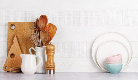 Kitchen utensils and cutting boards on table near white wooden wall, rustic home interior with copy...