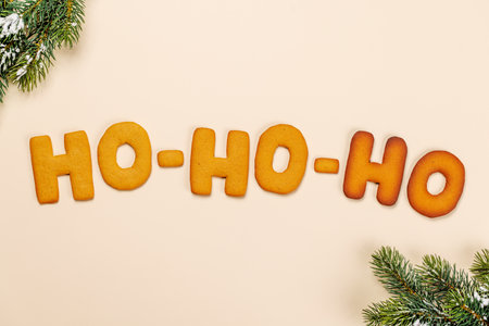 Ginger cookies shaped as Ho Ho Ho with fir branches on beige background, Christmas card styleの写真素材