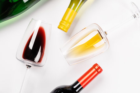 Wine glasses with red and white wine and bottles lying on white background, minimal elegant style with copy spaceの写真素材