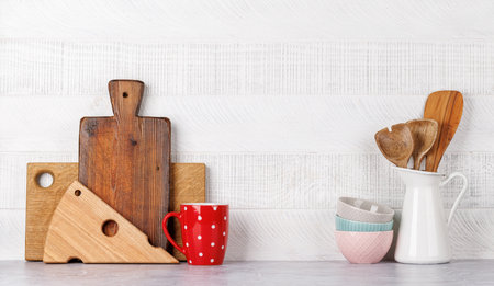Kitchen utensils and cutting boards on table near white wooden wall, rustic home interior with copy spaceの写真素材