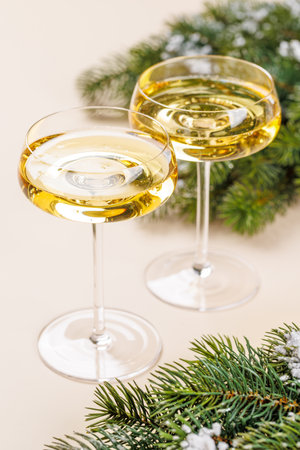 Two champagne glasses and snowy fir branches on beige background, Christmas card with copy spaceの写真素材