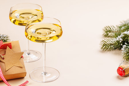 Two champagne glasses and snowy fir branches on beige background, Christmas card with copy spaceの写真素材
