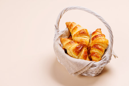 Freshly baked croissants in wicker basket on light background, cozy breakfastの写真素材
