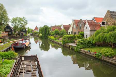 Charming Dutch village with small houses along a canal, calm rural scene with green nature and clear waterの写真素材