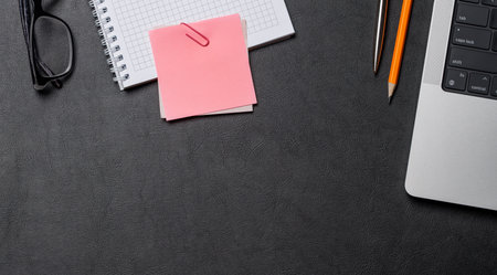 Office supplies and laptop on black leather workspace, top view with copy space, elegant background