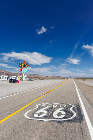 Amboy, California / United States - April 13 2023: The famous Route 66 road sign painted on asphalt with Roys Cafe, motel and gas station along the historic highway.のeditorial素材