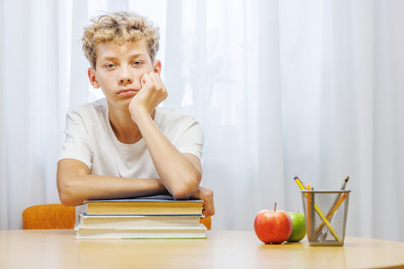 Schoolboy studying at home with notebook, and learning materials, looking thoughtful and confused