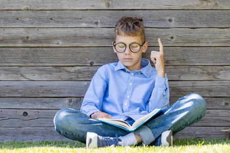 A boy reading a book on a grassy field.