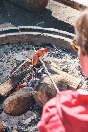 Woman fries sausages at the campfire outdoor. Woman Having Barbecue On Outdoor.