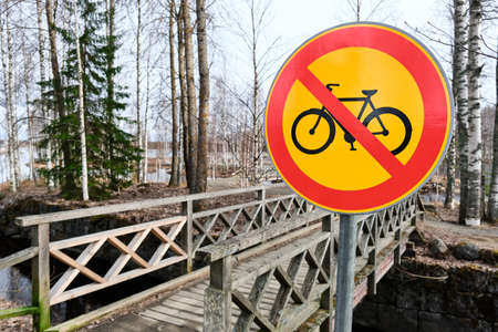 Yellow forbidden cycling road sign in Finland. The entrance of the park on the background.