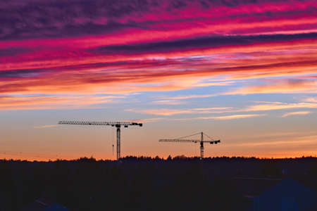 The tower cranes on the beautiful sunset sky background.