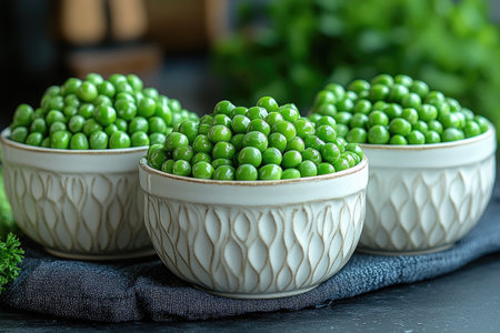 Three white bowls are overflowing with bright green peas on a dark gray surfaceの素材