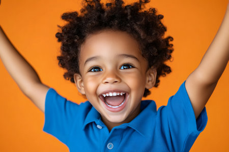 Portrait of a cheerful little boy with open arms screaming of joy on orange backgroundの素材