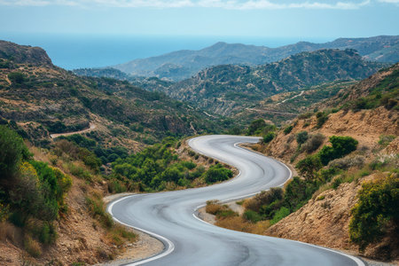 Winding asphalt road descends through the mountains towards the sea in Crete, Greeceの素材
