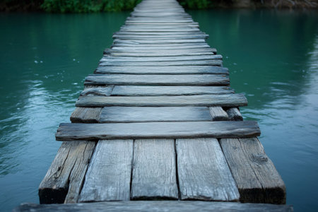 Old unstable wooden bridge crossing a river with turquoise waterの素材