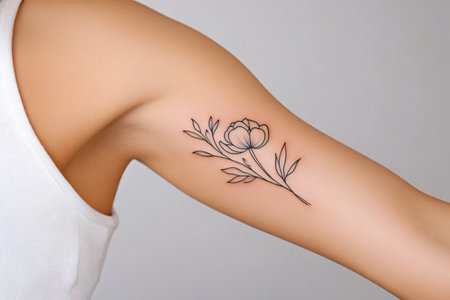 Minimalist floral tattoo graces a woman's arm, showcasing delicate linework and botanical beautyの素材
