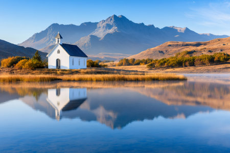 Small white church reflecting in a calm lake at the foot of a mountain range in autumnの素材