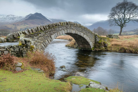 Stone bridge arches over tranquil river with misty mountains in the backgroundの素材