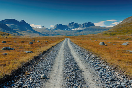 Gravel road stretches towards distant mountains under a clear blue skyの素材