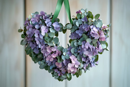 Beautiful heart shaped wreath hanging on white wooden wall, made with purple hydrangeas and eucalyptus leaves, perfect decoration for valentine's day or any romantic occasionの素材