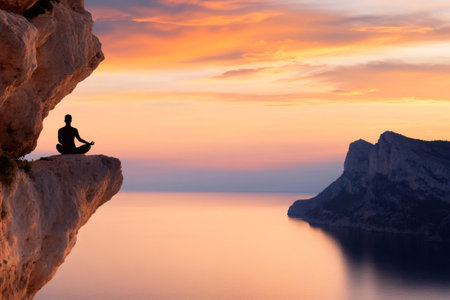 Silhouette of a man meditating on a cliff at sunset over the sea, finding inner peace and balanceの素材