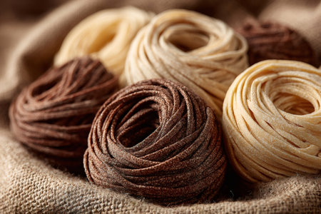 Close-up of colorful tagliatelle pasta nests resting on burlap, creating an appealing culinary sceneの素材