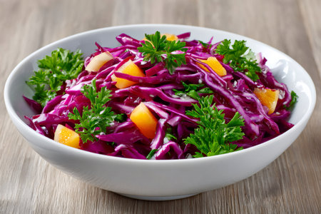 Red cabbage and chopped mango salad seasoned with fresh parsley in a white bowl on a wooden tableの素材