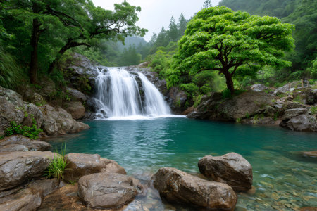 Beautiful waterfall flowing into a natural turquoise pond surrounded by lush green trees and rocks in a peaceful forestの素材